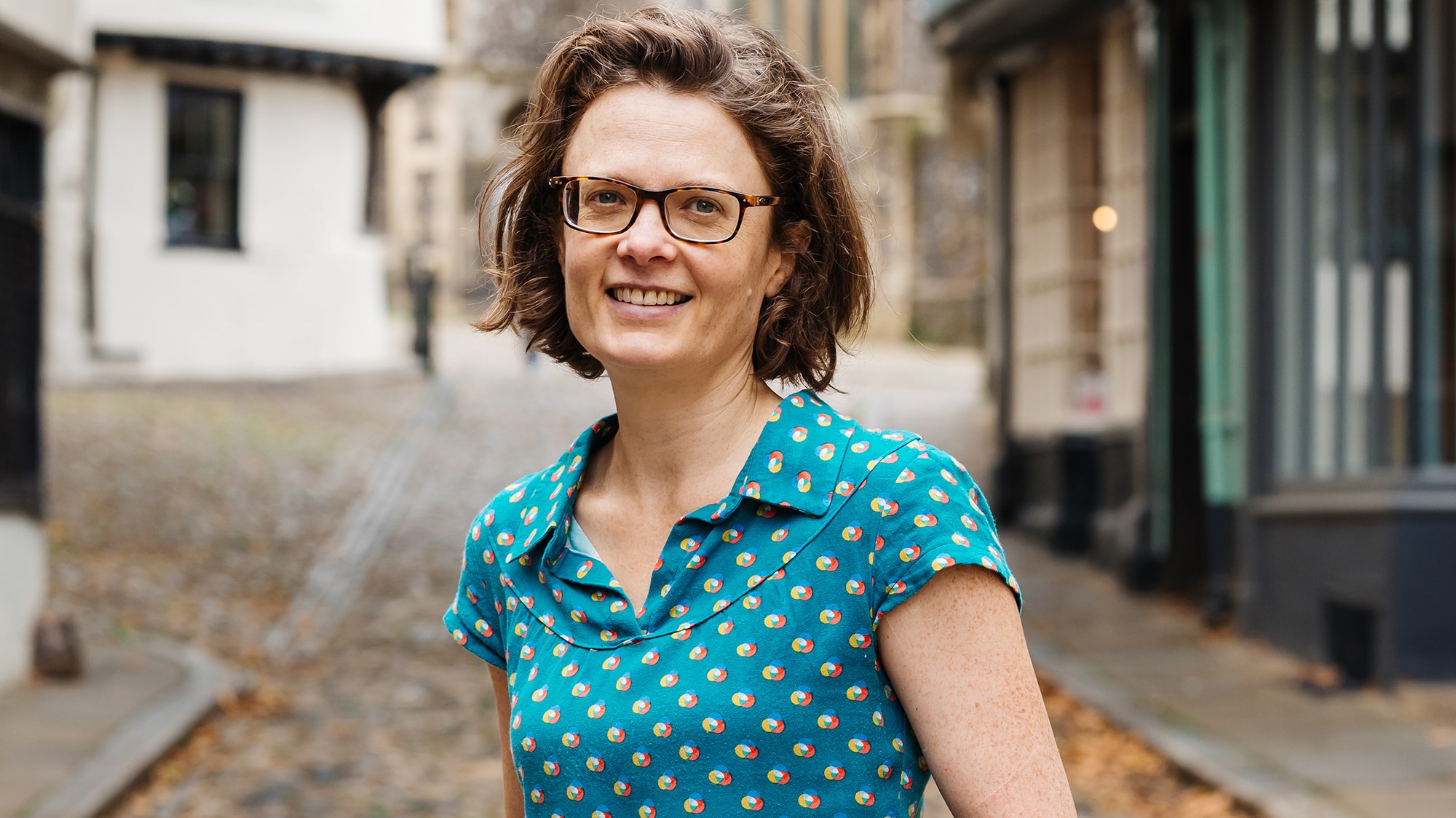 A photo of Julia, wearing a bright blue top, stood on a cobbled Norfolk street.